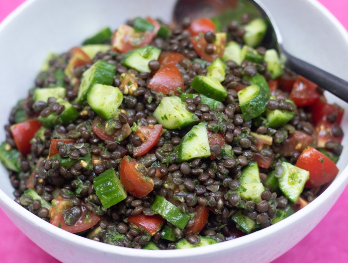 White bowl filled with black lentils, chopped cucumbers and tomatoes